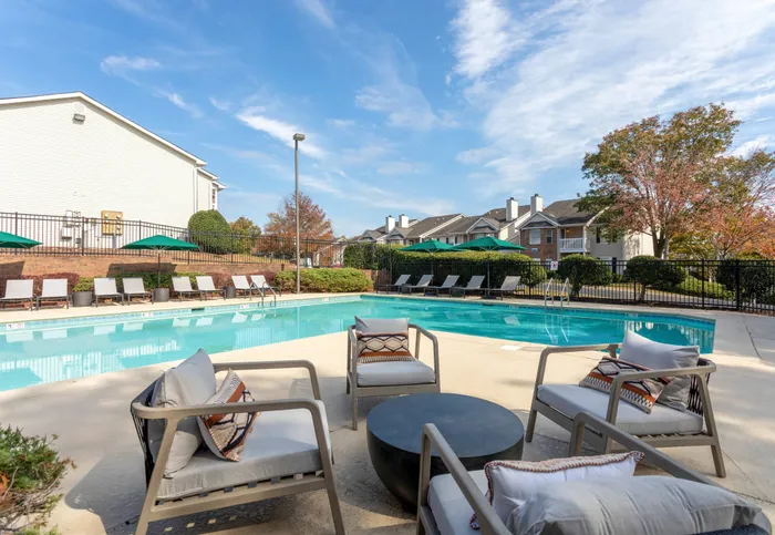 Outdoor pool with lounge seating, green umbrellas, and four outdoor arm chairs
