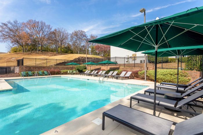 Pool, lounge seating, green umbrellas, looking out to trees and landscaping