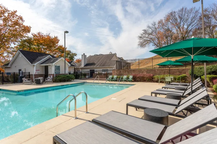 The pool area at our apartments near Belle Meade, TN, featuring beach chairs, umbrellas, and a view of the apartment complex.