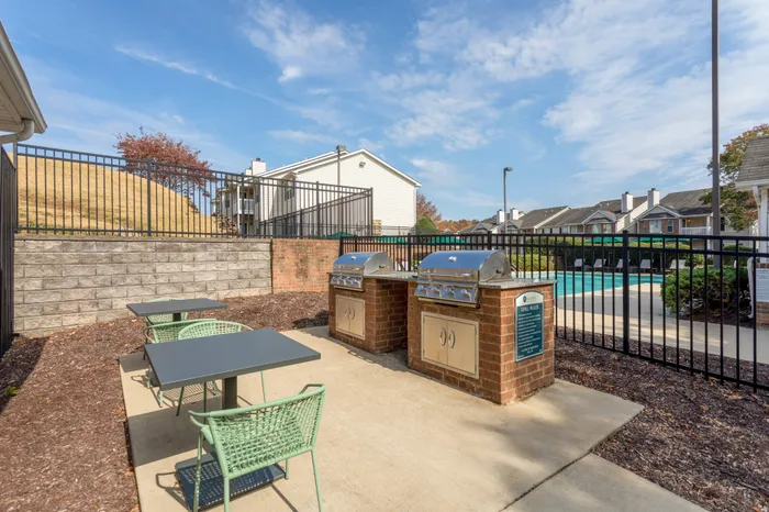 Two outdoor grills in built-in brick stands with a countertop, alongside outdoor dining tables and chairs besides the outdoor pool area
