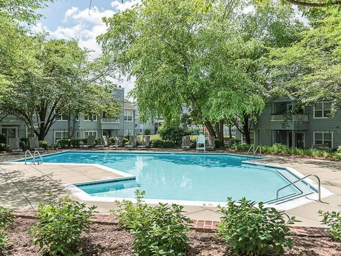 The pool area at our apartments for rent in Bowie, MD, featuring beach chairs in the shade under the large trees.