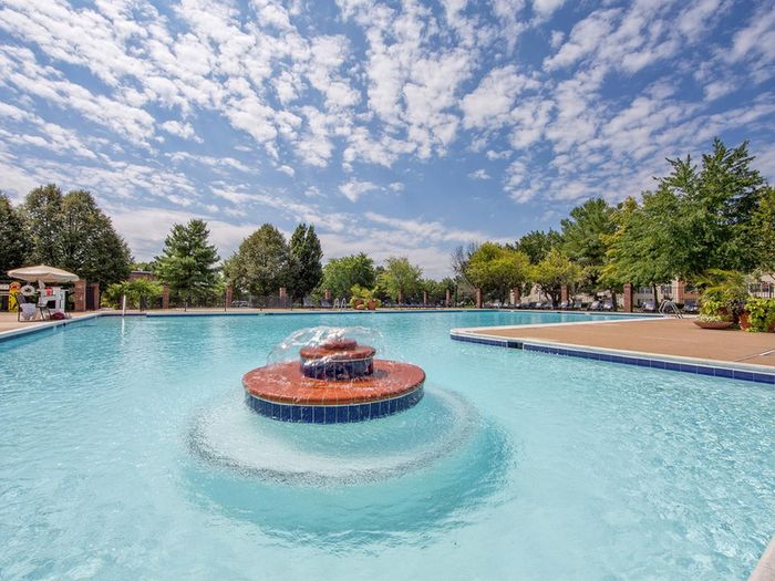 The pool at our apartments for rent in Leesburg, VA, featuring beach chairs, umbrellas, and a fountain.