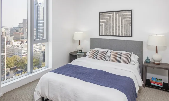 Model bedroom at our apartments in Portland, OR, featuring white and blue bedspread and floor to ceiling windows.