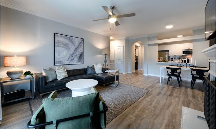Model living room at our apartments for rent in Herndon, VA, featuring wood grain floor paneling and a long grey couch.