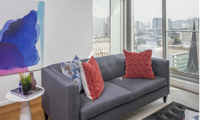 A dark grey couch with accent pillows by a window overlooking downtown Portland Oregon.