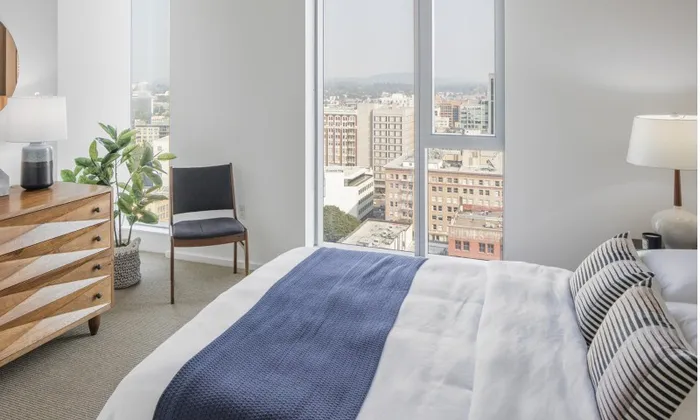 Model bedroom at our apartments in Portland, OR, featuring white and blue bedspread and floor to ceiling windows.