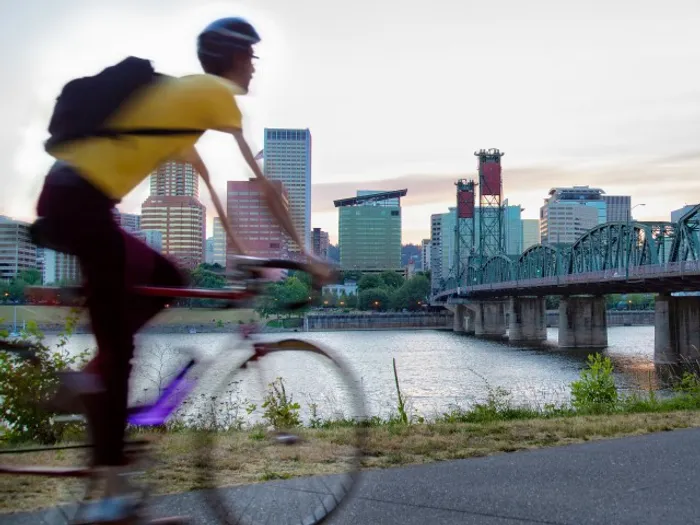 Man riding his bicycle with downtown Portland Oregon in the distance.