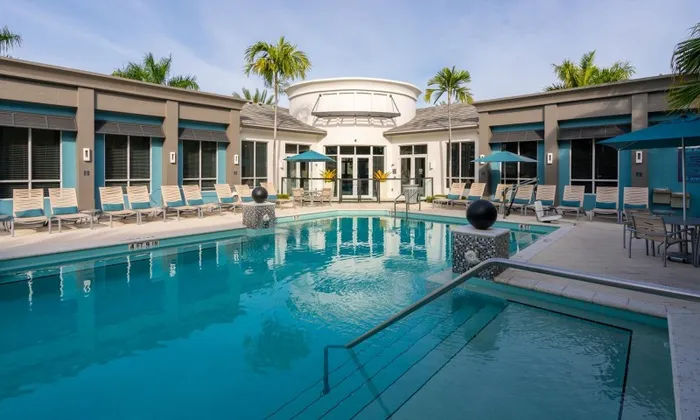 The pool area at our apartments in Delray Beach featuring beach chairs, umbrellas, and a clubhouse.