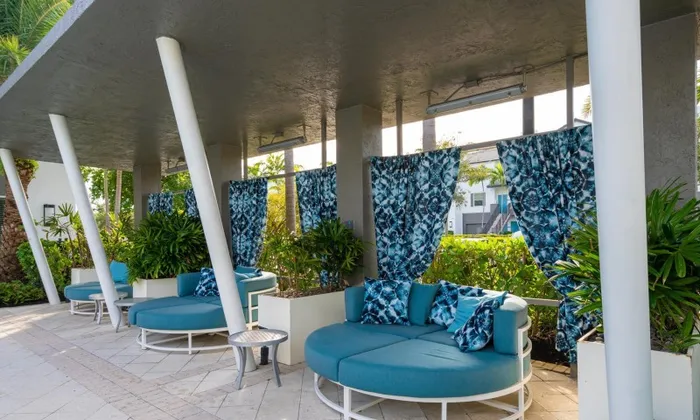 Outdoor lounge at our apartments in Delray, featuring cushioned blue chairs under a shade structure with palm trees.