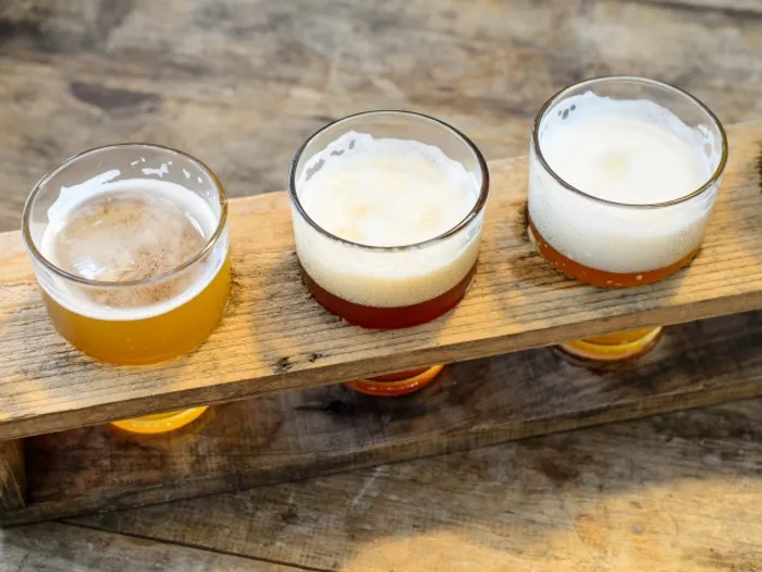 Stock photograph of three beers sitting in a wooden fleight. The beers are different colors but all have foam.