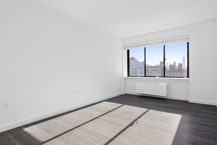 Empty room at our apartments in Midtown Manhattan, featuring wood grain floor paneling and a large window.
