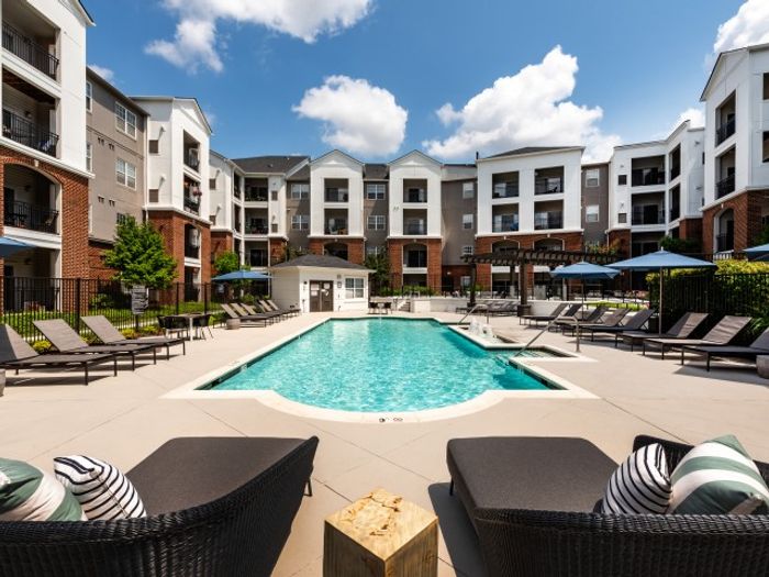 The pool area at our apartments for rent in Herndon, VA, featuring beach chairs, umbrellas, and a view of the apartments.