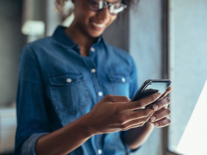 Someone standing holding their smartphone at our apartments for rent in Silver Spring. They are smiling and wearing denim.