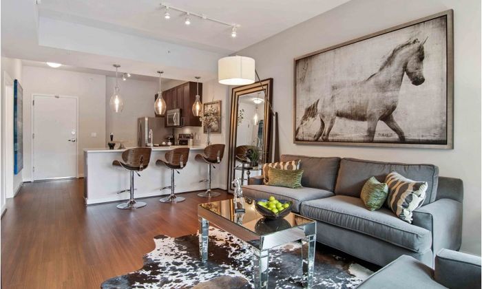 Model living room at our apartments for rent in Atlanta, featuring wood grain floor paneling and a view of the kitchen.