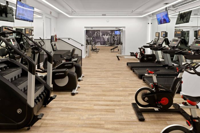 The fitness center at our apartments in Chelsea, featuring wood grain floor paneling and an array of exercise machines.