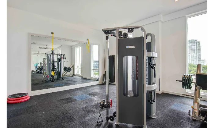 Fitness center at our apartments in Brickell, featuring assisted weight lifting machines, padded floors, and a mirrored wall.
