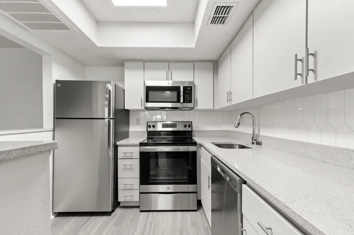 Model kitchen at our apartments in Clearwater, FL, featuring stainless steel appliances, grey counters, and white cubpboards.