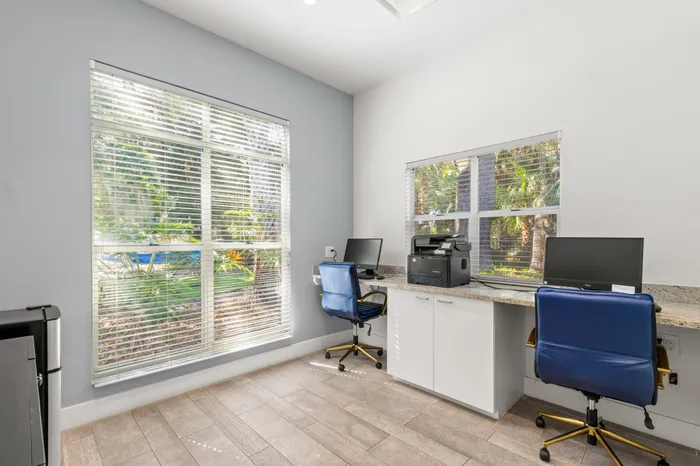 Business center with two desktops and large windows.