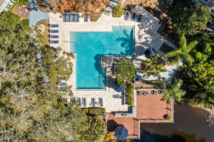 Outdoor pool with tiled flooring, seating, and surrounding trees.