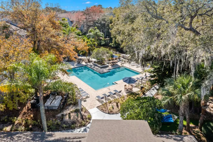 Outdoor pool with tiled flooring, seating, and surrounding trees.