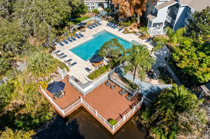 Outdoor pool with tiled flooring, seating, and surrounding trees.