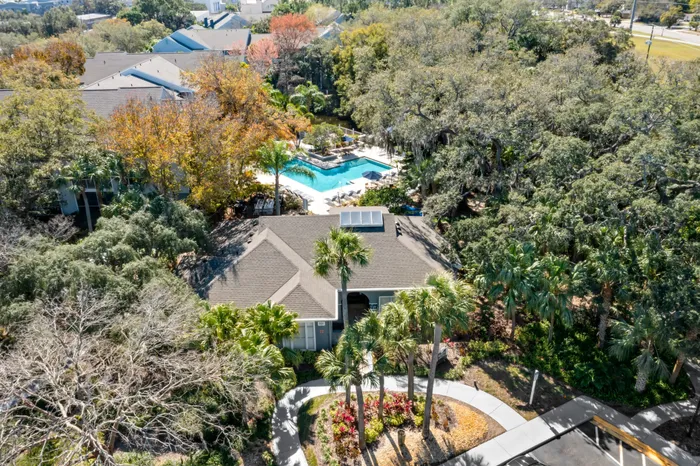 Outdoor pool with tiled flooring, seating, and surrounding trees.