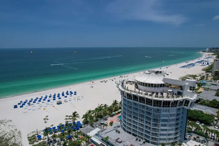 Aerial view of the beach near our apartments for rent in Clearwater, FL, featuring umbrellas, skyscrapers, and the ocean.