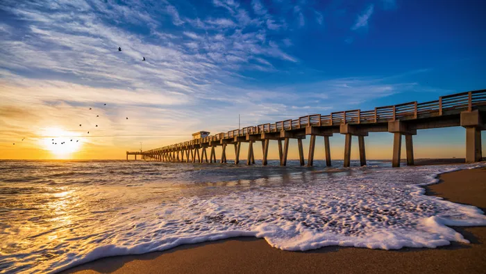 A pier near our apartments for rent in Clearwater, FL, featuring the sunset and waves crashing on the beach.