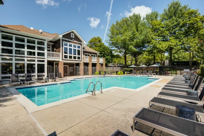 The pool area at our apartments for rent in Owings Mills, MD, featuring beach chairs, umbrellas, and trees.
