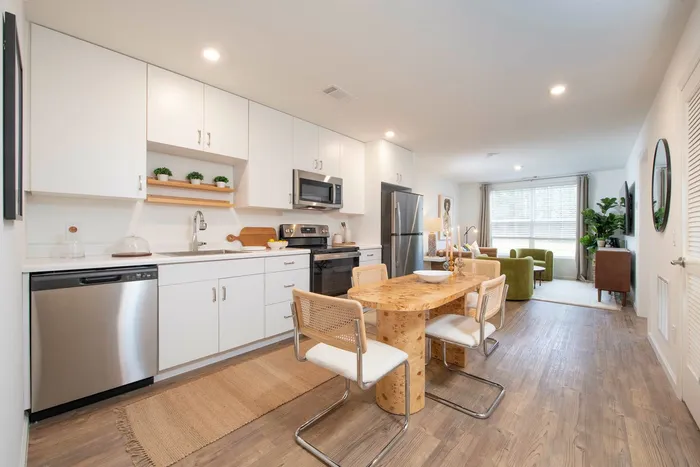 Dining and living areas inclduing white kitchen cabinets and large window.