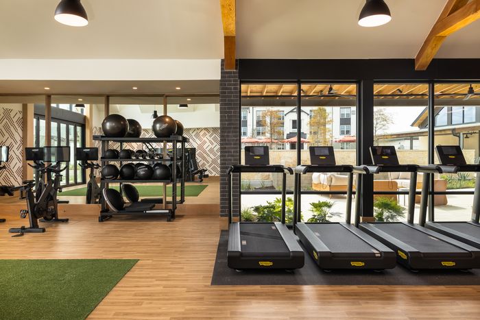 Fitness center treadmills facing tall windows at The Prado apartments in Del Valle, TX