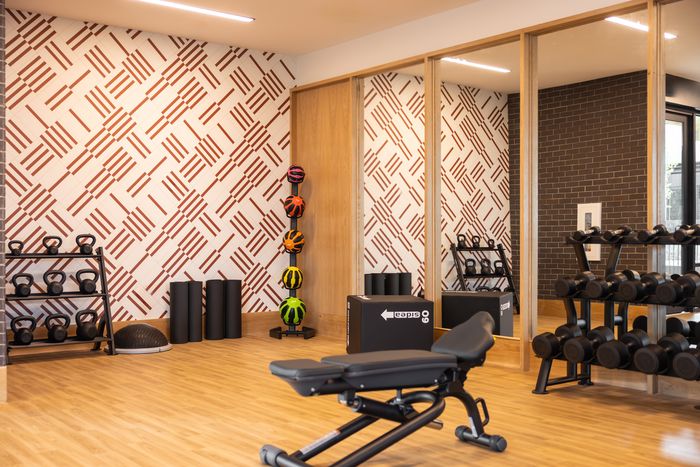 Free-weight area with dumbbells and patterned wall at The Prado apartments in Del Valle, TX
