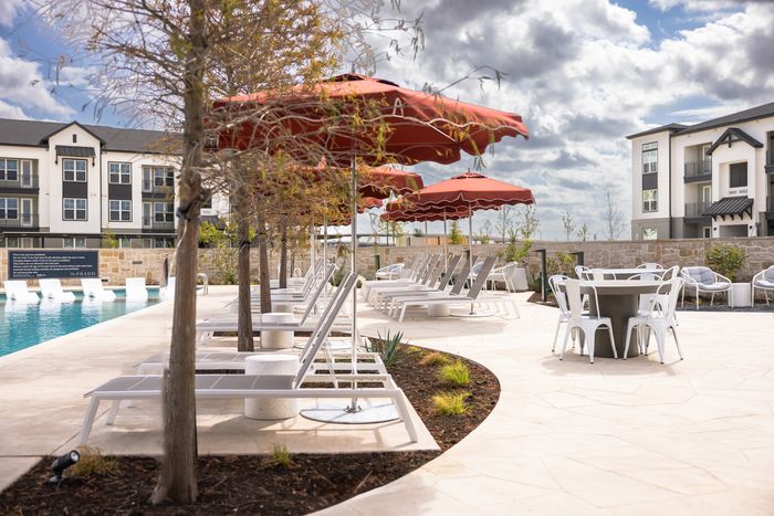 Pool courtyard with red umbrellas and lounge chairs at The Prado apartments in Del Valle, TX