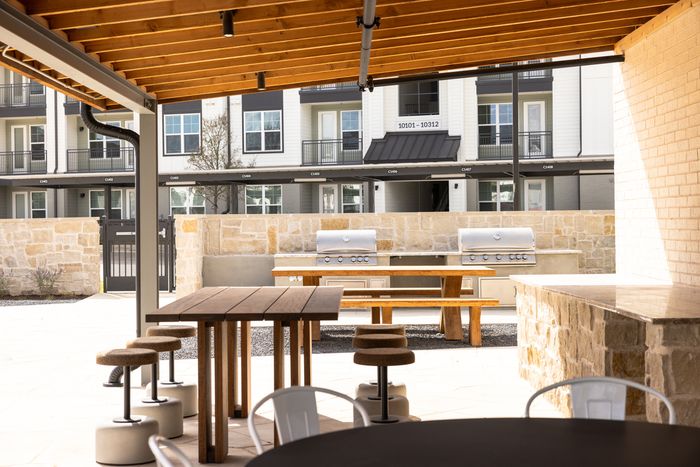 Covered outdoor grill area with dining tables at The Prado apartments in Del Valle, TX
