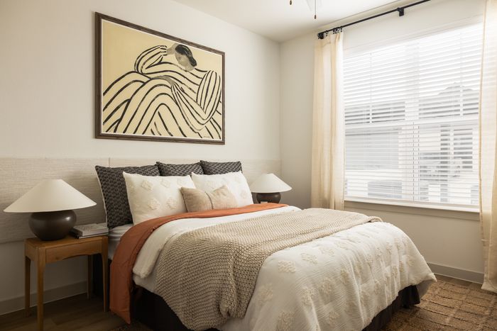 Apartment bedroom with plush bed and large window at The Prado apartments in Del Valle, TX