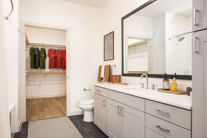 Apartment bathroom with long vanity and closet access at The Prado apartments in Del Valle, TX