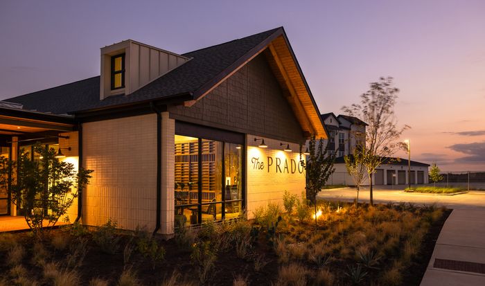 Clubhouse exterior lit at dusk at The Prado apartments in Del Valle, TX