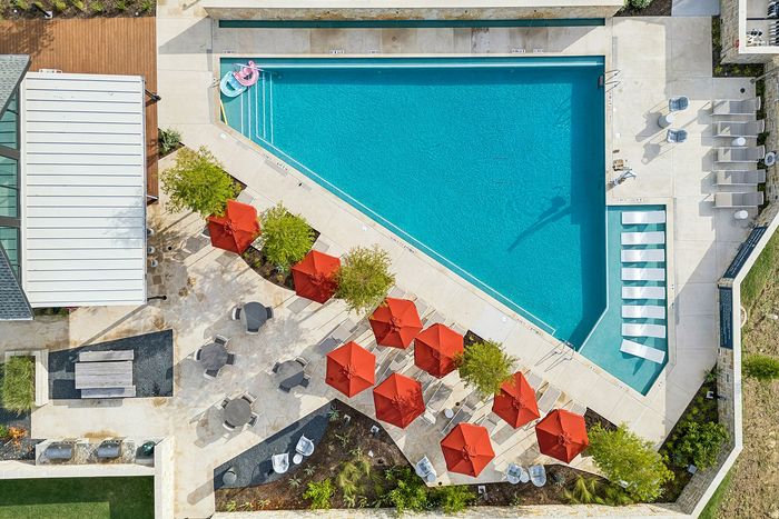Aerial view of pool with red umbrellas and lounge chairs at The Prado apartments in Del Valle, TX