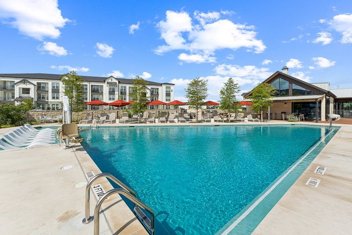 Resort-style pool with sunny deck and lounge chairs at The Prado apartments in Del Valle, TX