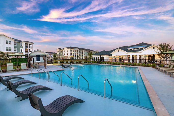 Resort-style apartment swimming pool with poolside lounge chairs and scenic sunset views.