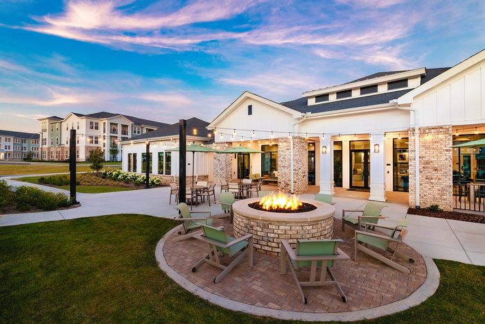 Outdoor fire pit with circular seating area, landscaped surroundings, and apartment community views at sunset.
