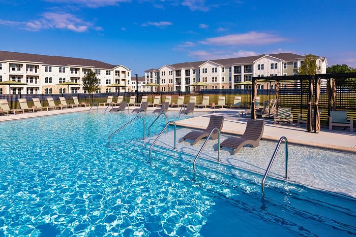 Resort-style outdoor apartment swimming pool surrounded by lounge chairs, landscaped grounds, and community amenities.