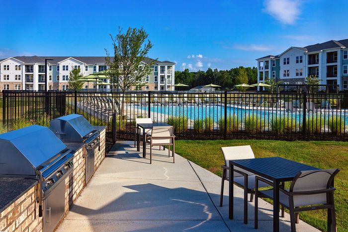 Outdoor grilling station with built-in grills, countertop space, and seating near the apartment community pool.