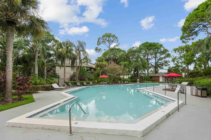 The pool area at our apartments for rent in Clearwater, FL, featuring beach chairs, umbrellas, and a hot tub.