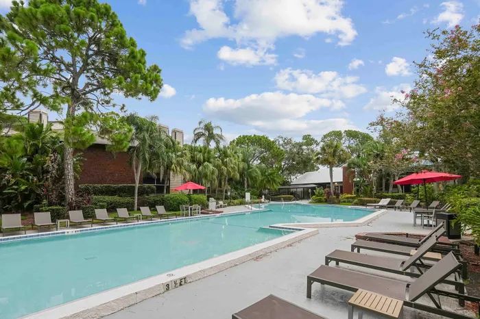 The pool area at our apartments for rent in Clearwater, FL, featuring beach chairs, umbrellas, and a hot tub.