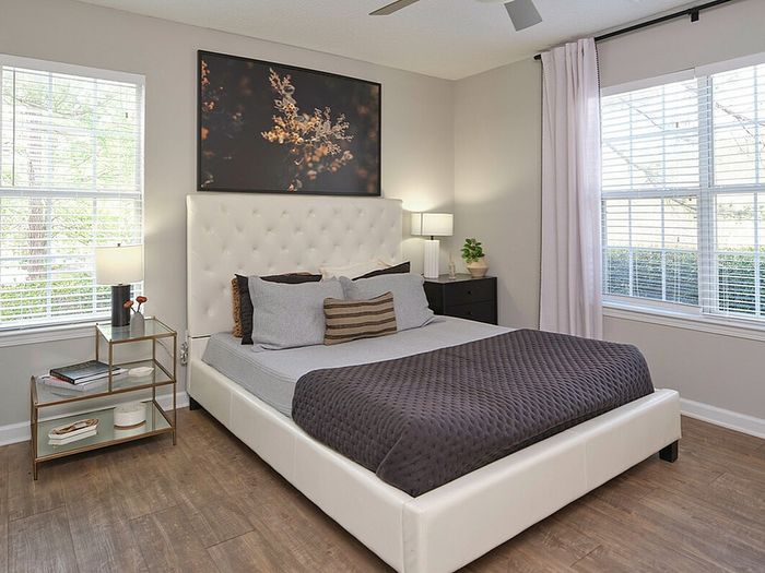 Inviting bedroom with elegant decor, featuring natural light streaming through large windows, a plush white bed, and sleek wooden flooring.