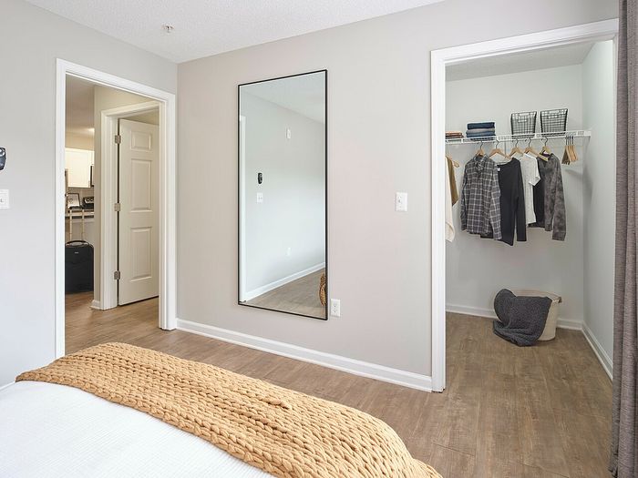 Modern bedroom with a spacious walk-in closet, featuring sleek wooden flooring and a large mirror, enhancing the room's elegance.