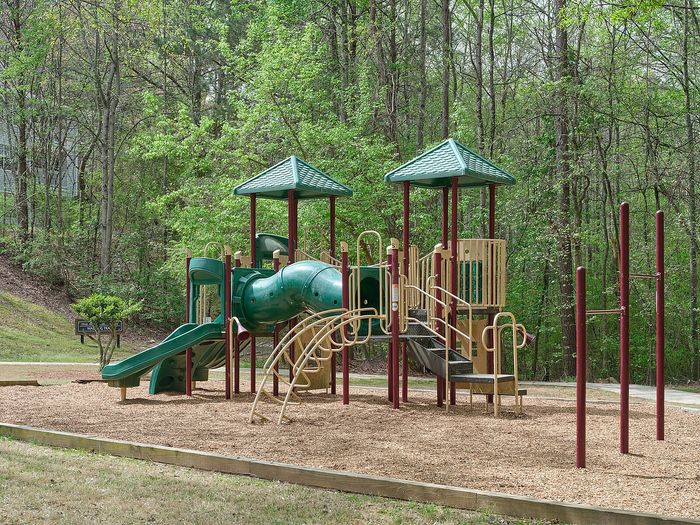 Charming playground nestled among lush trees, featuring slides and climbing structures, perfect for family enjoyment.