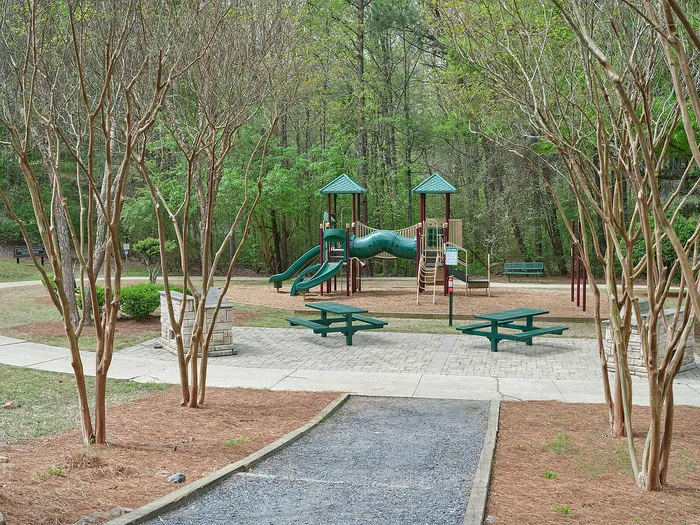 Serene apartment complex playground featuring vibrant green slides, charming picnic tables, and lush wooded surroundings.