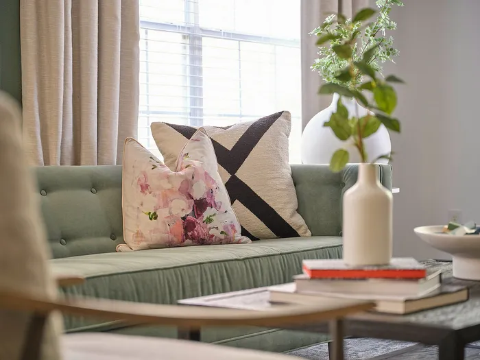 Elegant living room with a plush green couch, artfully arranged pillows, and a chic vase with greenery, bathed in natural light.